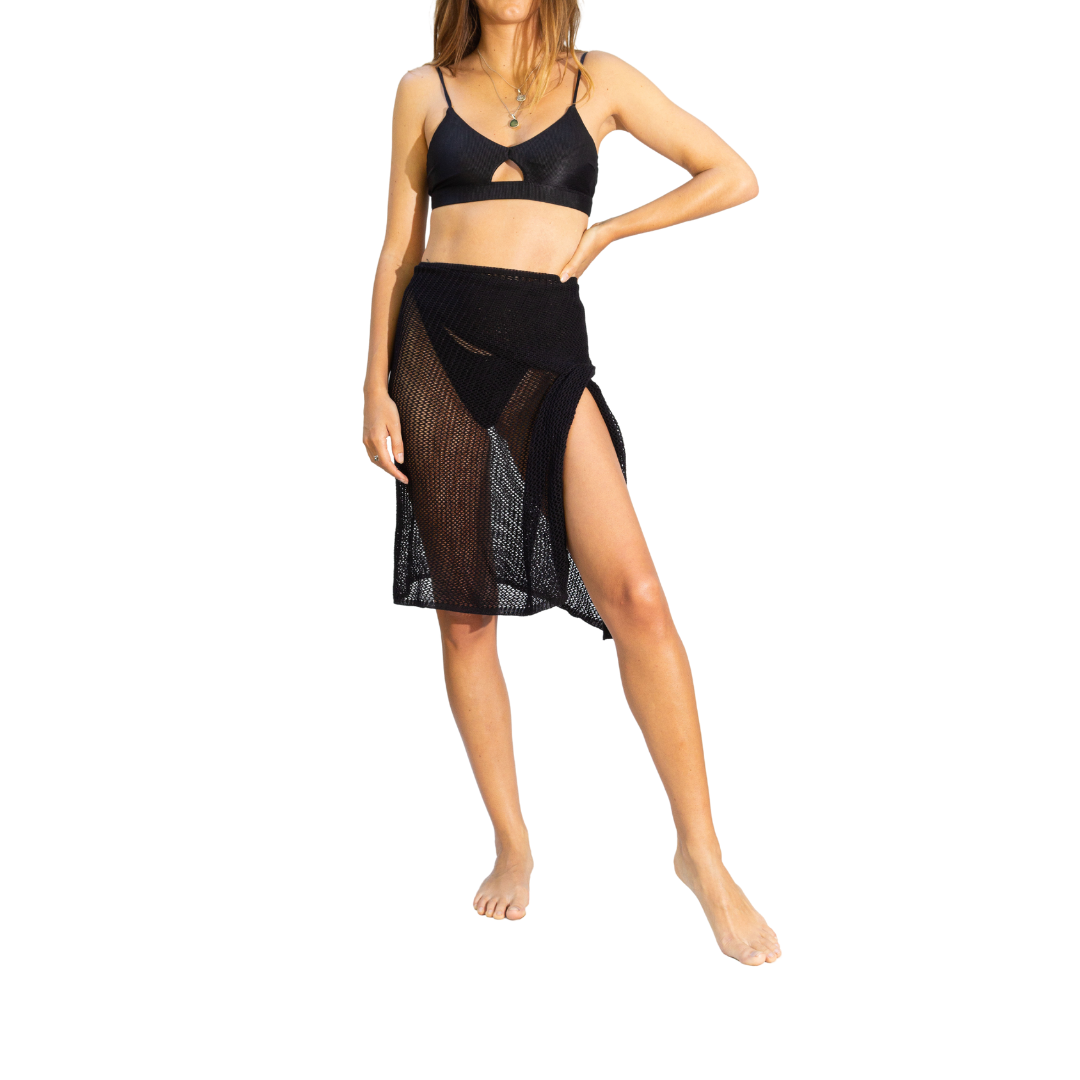 A woman standing wearing a stylish black crochet cover-up, layered over her swimsuit, showcasing a beachwear look from the front