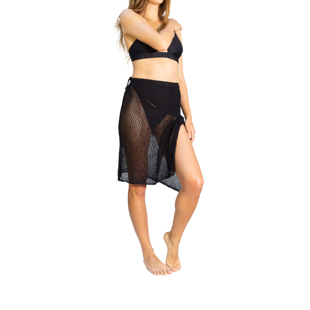A woman standing  wearing a stylish black crochet cover-up, layered over her swimsuit, showcasing an elegant beachwear look