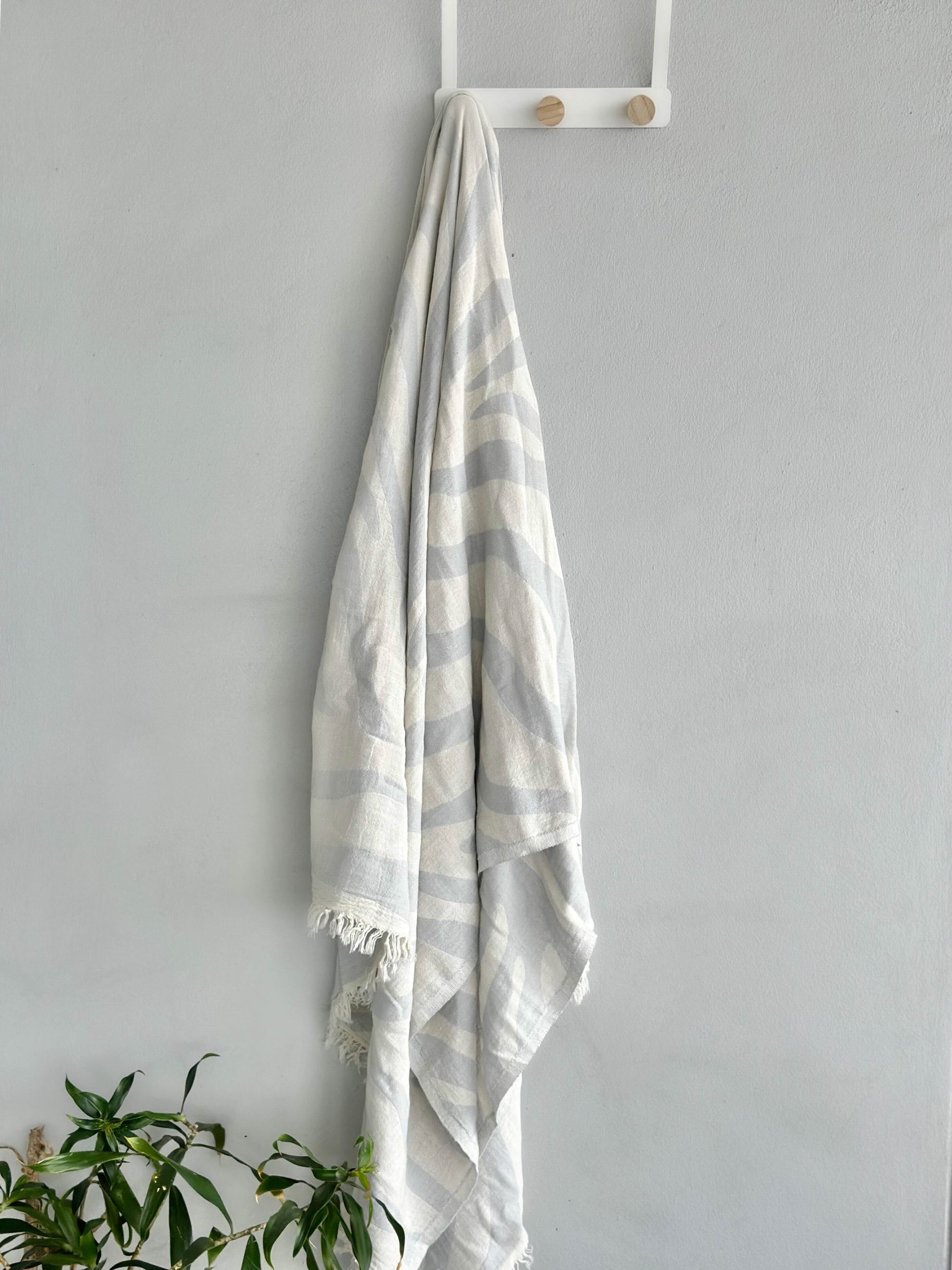 A light blue beach towel hanging on a stand, showcasing its vibrant color and patterns, ready for a day at the beach or poolside relaxation.